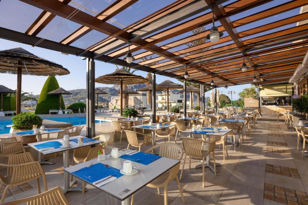 Atvērta restorāna terase ar modernām mēbelēm, zilu galda piederumu un peldbaseinu fonā, radot relaksējošu atmosfēru. Ideāli piemērota maltītēm ārā.