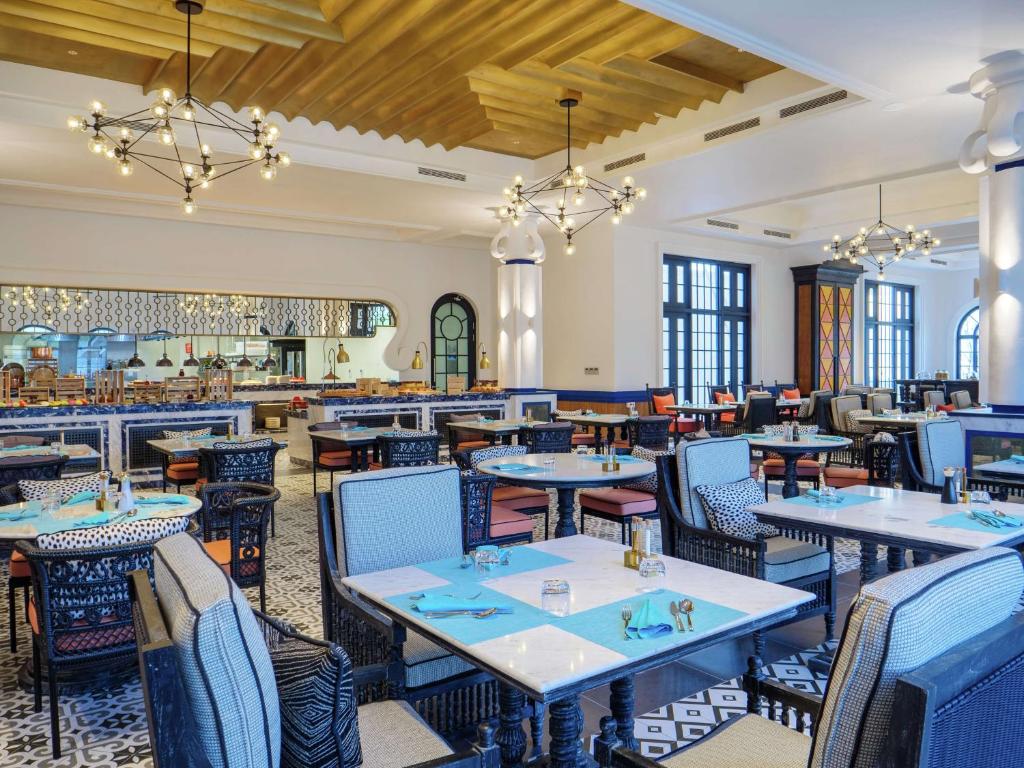 Mūsdienīgs restorāns ar elegantu interjeru, kas ietver stilīgas mēbeles un pievilcīgu apgaismojumu. Galdi ir sakārtoti ar krāsainiem salvešu komplektiem un galda piederumiem, radot patīkamu atmosfēru.