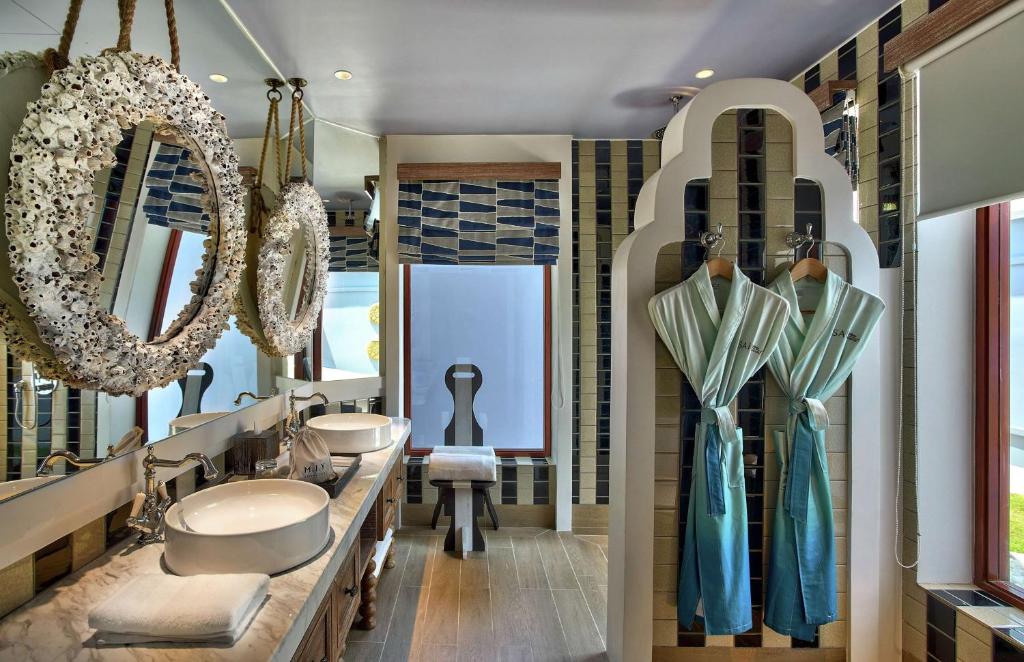 Moderns vannas istabas interjers ar divām vannas izlietnēm, apgaismojumu un dekoratīviem spoguļiem, kas izrotāti ar čaulām. Svaigi zili halāti ir pakārti uz stilizētas drēbju pakaramā.