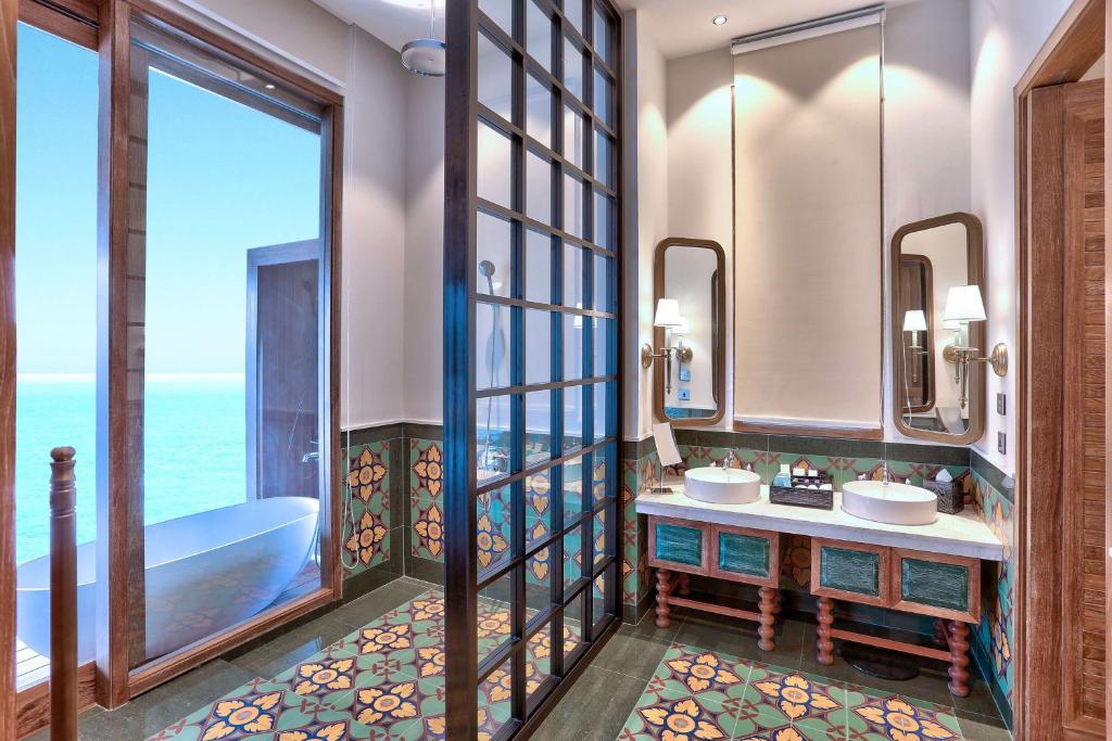 Mūsdienīga vannas istaba ar skatu uz jūru, dekorēta ar krāsainām flīzēm un elegantu vannu. Stils apvieno klasiskus elementus ar modernām detaļām.