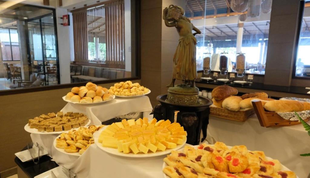 Bufete ar dažādiem maizīšu un desertu izstrādājumiem, tostarp sieriem un saldumiem, rotāta ar statuju vidū. Ideāla ainava brokastīm vai svinībām.