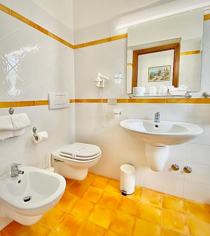 Gaiša un moderna vannas istaba ar oranžiem flīzēm, izlietni un bidē, kā arī spoguli un higiēnas piederumiem.