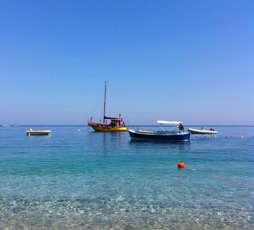 Skaista pludmales ainava ar vairākām laivām mierīgā ūdenī, kas atspoguļo skaidro debesi.