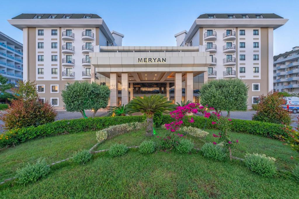 Meryan Hotel ieeja ar ziedošiem krūmiem un modernu arhitektūru.