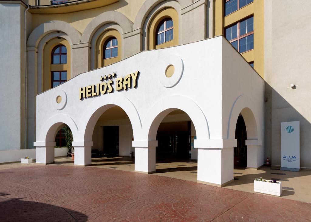 Helios Bay viesnīcas ieeja ar elegantu arhitektūru un izteiksmīgu logo, kas atrodas viesmīlīgā vidē. Ideāla vieta atpūtai un brīvdienām.