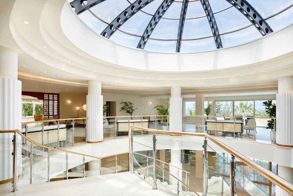 Mūsdienīga interjera telpa ar aplīmētu griestu konstrukciju un stikla jumtu, kas nodrošina dabisko apgaismojumu. Telpā ir eleganta kāpņu konstrukcija un augi, kas piešķir dzīvīgumu.