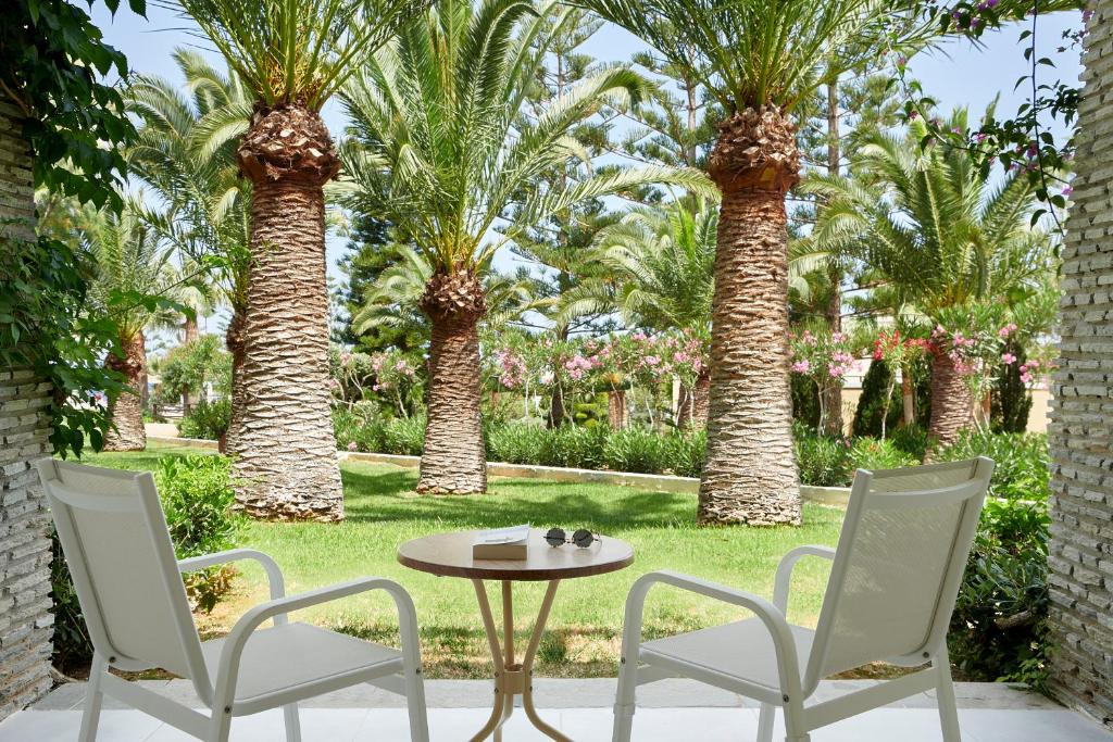 Ainava ar palmām un atpūtas krēsliem, kas izvietoti pie galda, sniedz mierīgu atmosfēru un dārza skaistumu. Ideāla vieta relaksācijai un dabas baudīšanai.