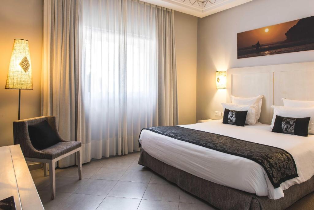 Mājīgs viesnīcas numurs ar divguļamo gultu, elegantām lampām un ērtiem krēsliem, kas nodrošina relaksējošu atmosfēru. Lieli logi ļauj ieplūst dabiskai gaismai.
