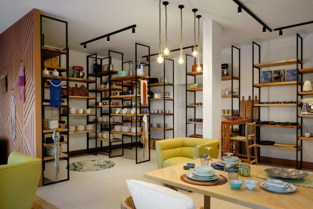 Mūsdienīga interjera veikaliņa iekārtojums ar stilīgām plauktiem, kas satur traukus un virtuves piederumus. Dzeltena dīvāna un koka galda kombinācija rada mājīgu atmosfēru.