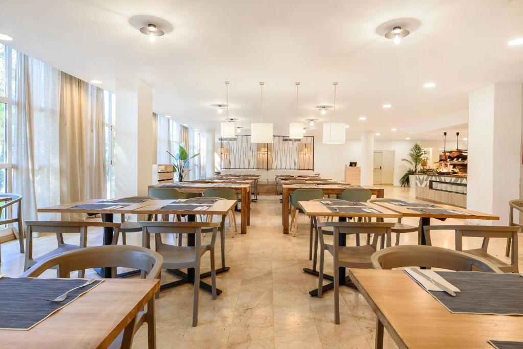 Mūsdienīgs restorāns ar koka galdiem un krēsliem, gaišu interjeru un plašiem logiem, kas nodrošina dabīgu apgaismojumu. Eleganti galdi ir sagatavoti ar galdautiem un galda piederumiem.