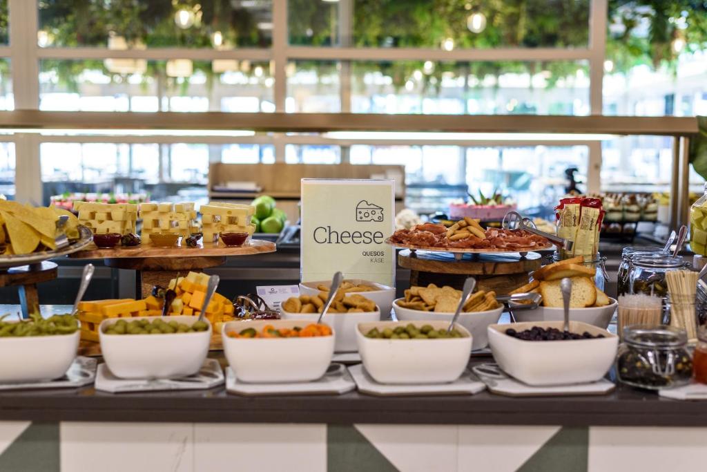 Siera bufete ar dažādām siera šķirnēm un uzkodām, ieskaitot olīvas un dārzeņus. Galds ir dekorēts ar zīmi "Cheese" un piedāvā plašu izvēli gardumiem.