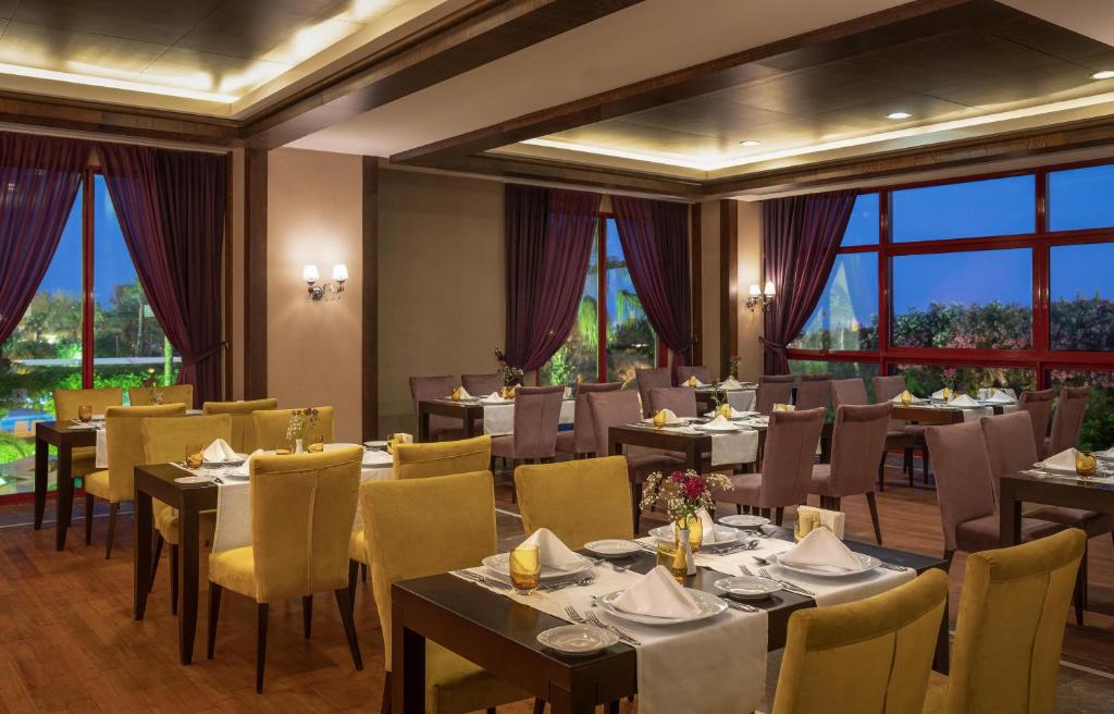 Kaya Belek restorāns ar elegantiem galdiem un skatu uz dārzu