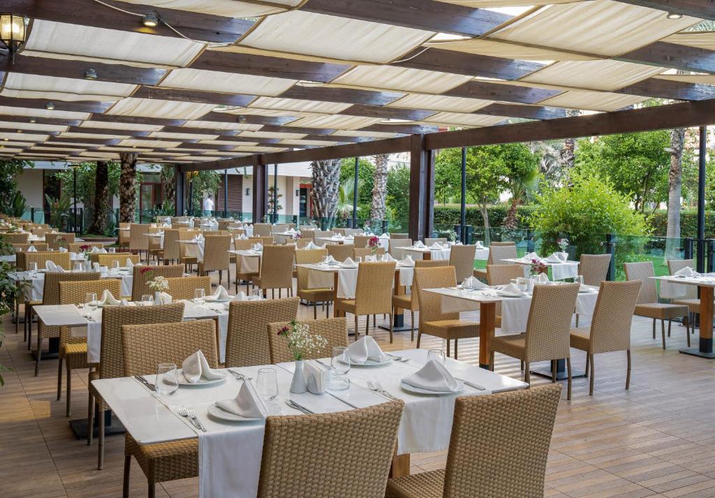 Kaya Belek restorāns ar elegantām galdiem un zaļiem augiem apkārt.