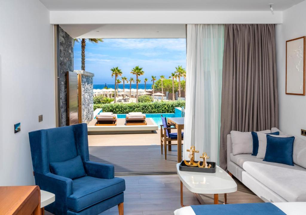 Mūsdienīgs viesnīcas numurs ar skatu uz baseinu un okeānu, iekārtots ar ērtām mēbelēm un lieliem logiem, kas nodrošina dabīgu apgaismojumu.