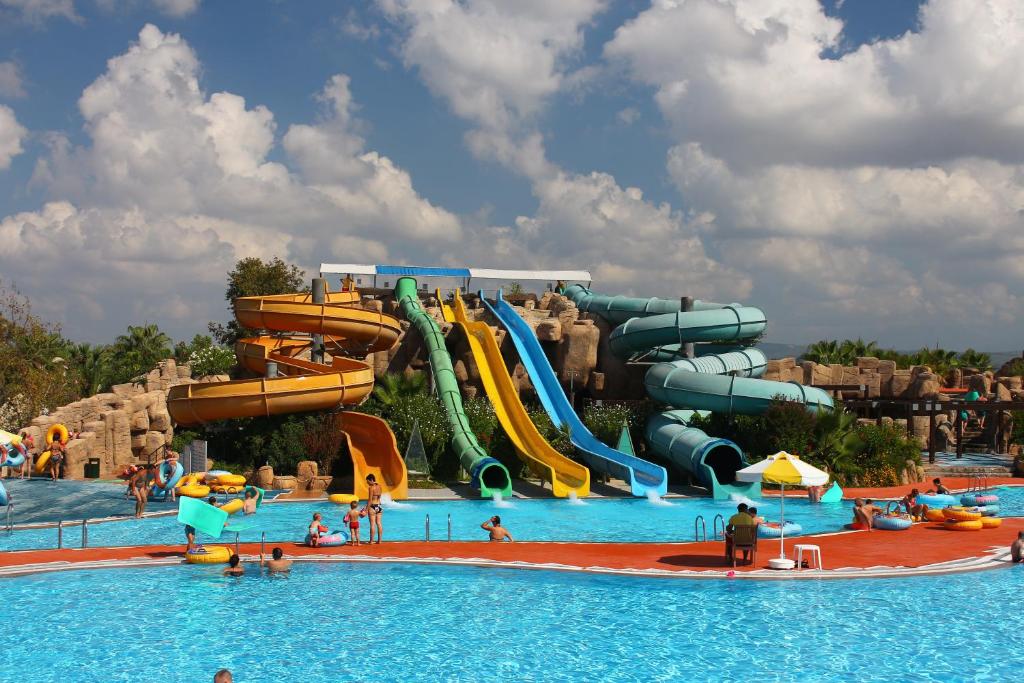 Ūdens atrakciju parks ar dažādiem slidkalniņiem un peldbaseinu, kur apmeklētāji izbauda ūdens priekus. Debesis ir skaidras ar dažām mākoņu pūkām.