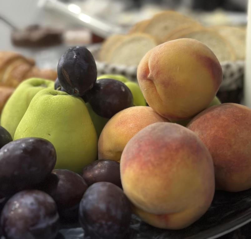 Svaigu augļu kompozīcija ar zaļām āboliem, persikiem un sliņķiem, kas pasniegti uz melnas plāksnes. Ideāls attēls veselīgai uzkodu izvēlei.