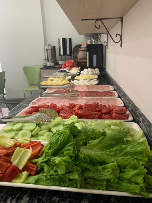 Svaigu dārzeņu un gaļas uzkodu bārs, kurā redzami tomāti, gurķi, salātlapas, paprika, šķiņķis un cietais siers. Aiz bāra ir kafijas automāts un dažādas citas uzkodas.