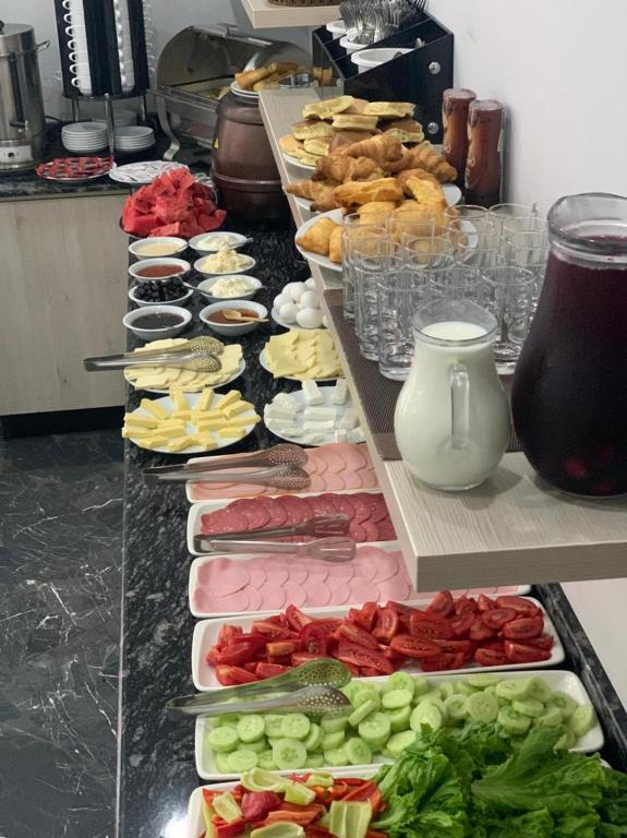 Bagātīgas brokastu bufetes izkārtojums ar dažādiem ēdieniem, tostarp maizēm, sieriem, gaļām, dārzeņiem un dzērieniem. Ideāls priekšstats par veselīgu un daudzveidīgu maltīti.