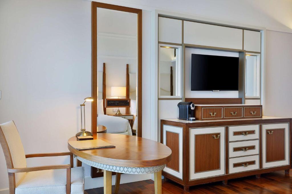 Mūsdienīgs viesnīcas numura interjers ar koka mēbelēm, televizoru un galdu. Uz galda atrodas lampiņa un kafijas automāts.