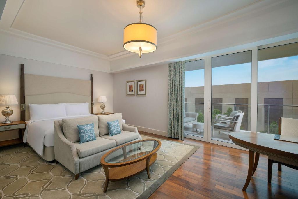 Mūsdienīga viesnīcas numura iekārtojums ar ērtu gultu, dīvānu un balkonu, kas piedāvā skatu uz dārzu. Interjers ir gaišs un elegants, ar koka grīdu un stilīgu apgaismojumu.