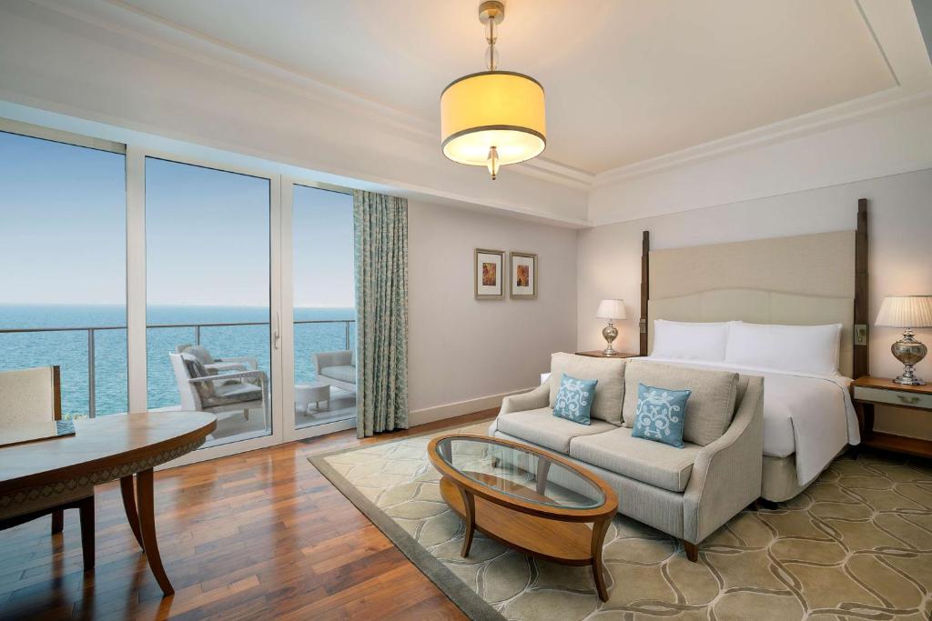 Elegants numurs ar skatu uz jūru, kurā ir moderna mēbeļu iekārtojums, ērta sofa un liels logs, kas nodrošina dabīgu apgaismojumu.