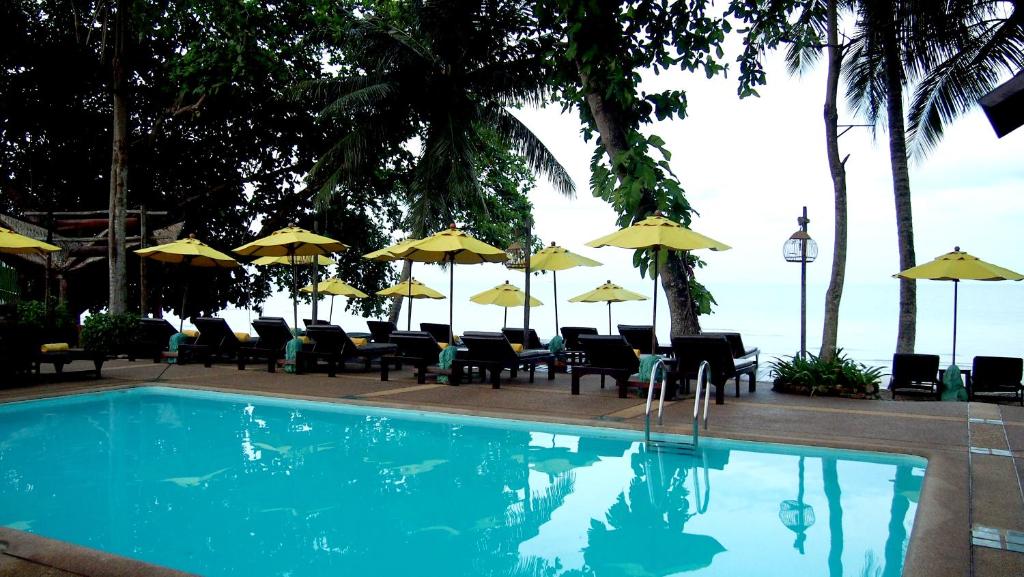 Peldbaseins pie Banpu Koh Chang ar sauļošanās krēsliem un lietussargiem piekrastē.