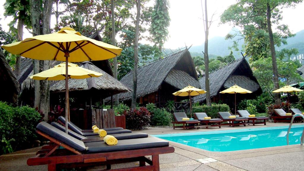 Peldbaseins pie Banpu Koh Chang ar sauļošanās krēsliem un dzeltenām parasolēm.