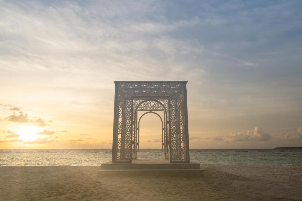 Saulriets pie Ifuru Island Maldives pludmales ar dekoratīvu arku.