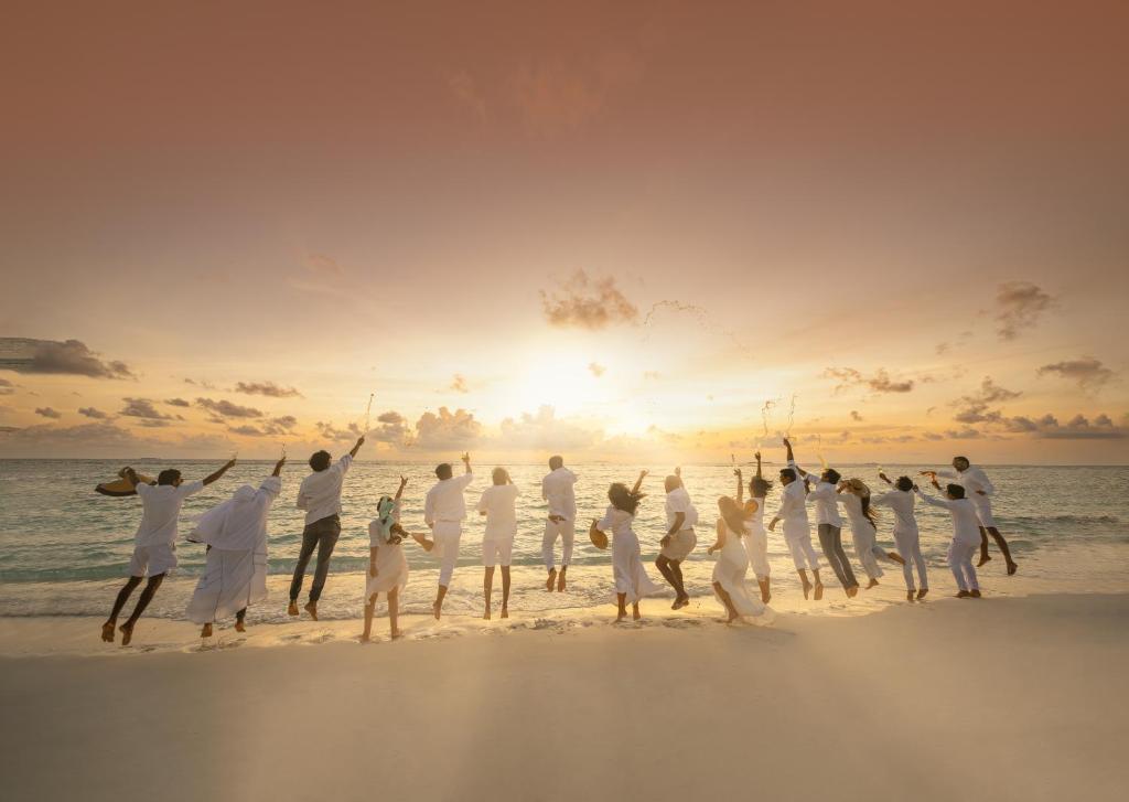 Grupa cilvēku baltos tērpos priecājas pie Ifuru Island Maldives pludmales saulrieta laikā.