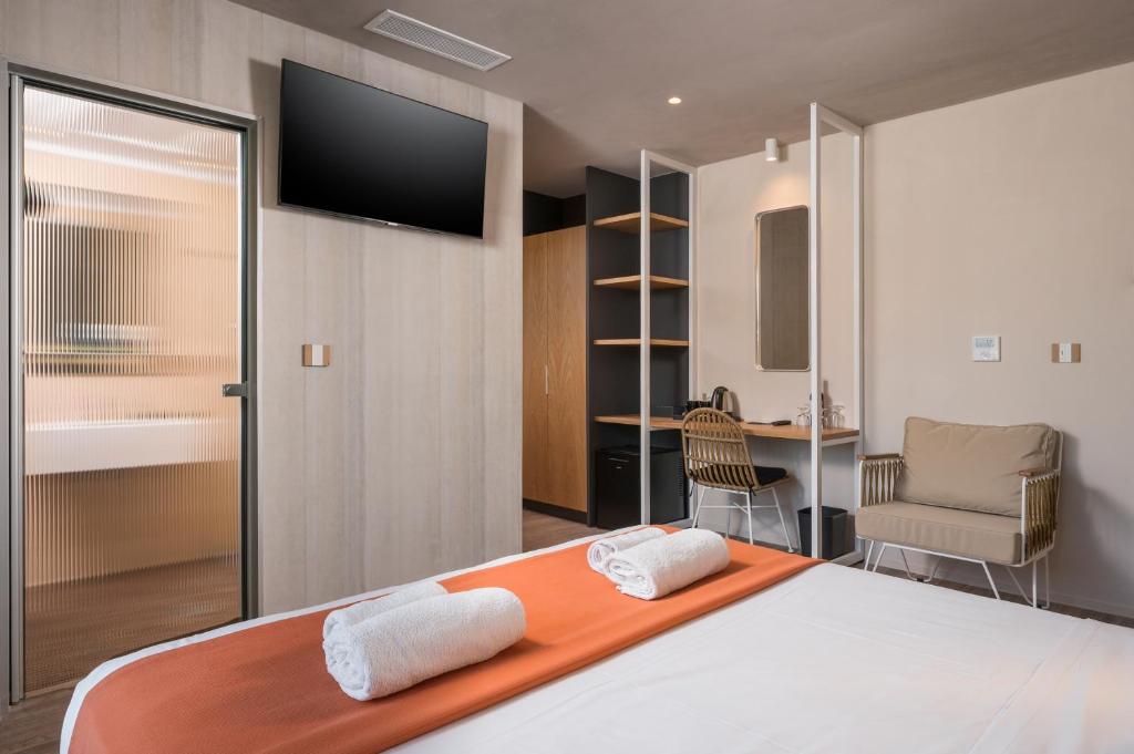 Moderns viesnīcas numurs ar ērtu gultu, televizoru un atpūtas zonu, kurā ir krēsls un galds. Numurā ir arī plaukti un stikla durvis uz vannas istabu.