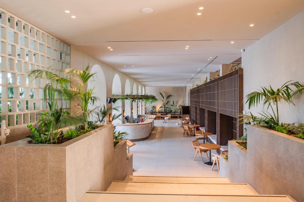 Mūsdienīga viesnīcas interjera telpa ar plašu kāpņu telpu, augiem un ērtām sēdvietām. Gaismas elementi rada patīkamu atmosfēru.