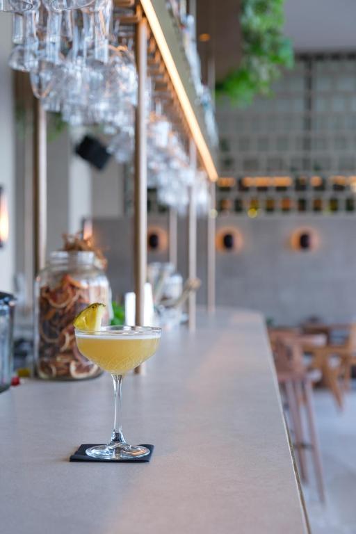 Eksotiska kokteiļa glāze ar citrona šķēlīti uz bāra letes, fona ir eleganta bāra vide ar glāzēm un dekoratīviem elementiem.