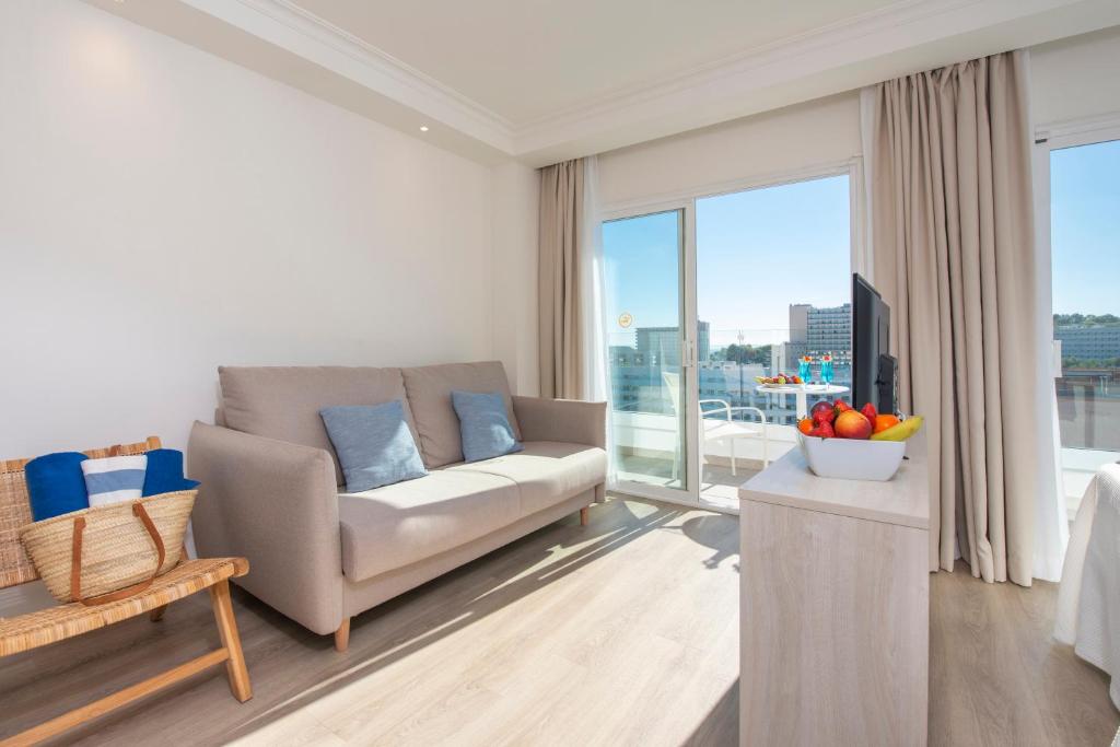 Mūsdienīga viesnīcas istaba ar gaišu interjeru, ērtiem dīvāniem un skatu uz terasi, kurā ir augļi un dzērieni. Ērts un viesmīlīgs atmosfēra atpūtai.