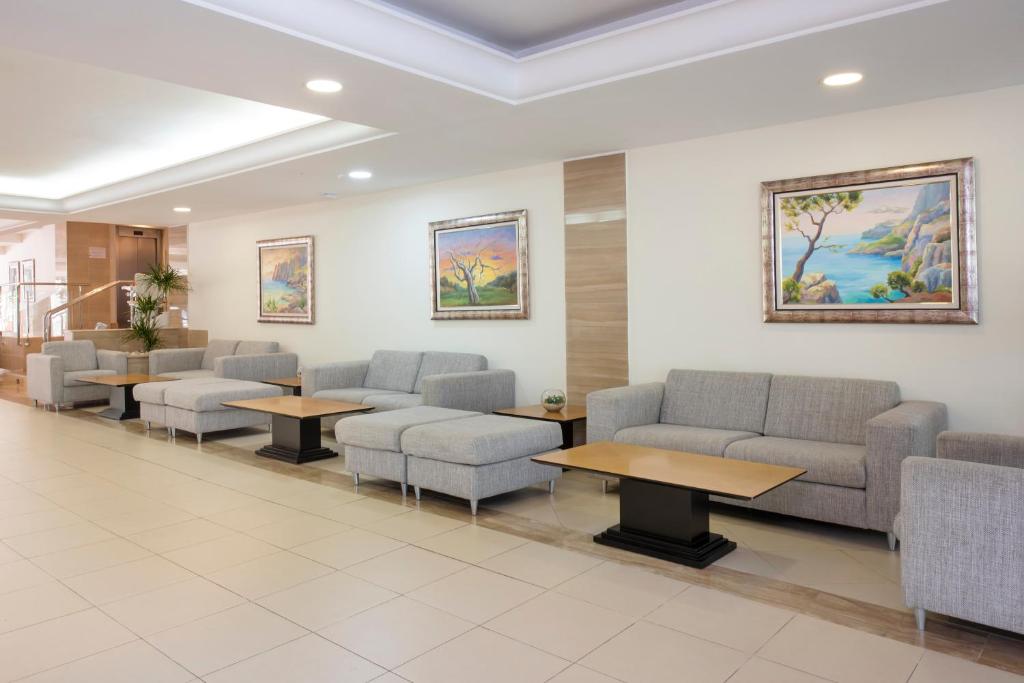 Mūsdienīgs viesnīcas hols ar pelēkiem dīvāniem un koka galdiem, pie sienām gleznas ar ainavām. Telpa ir gaiša un plaša, radot komfortablu atmosfēru.