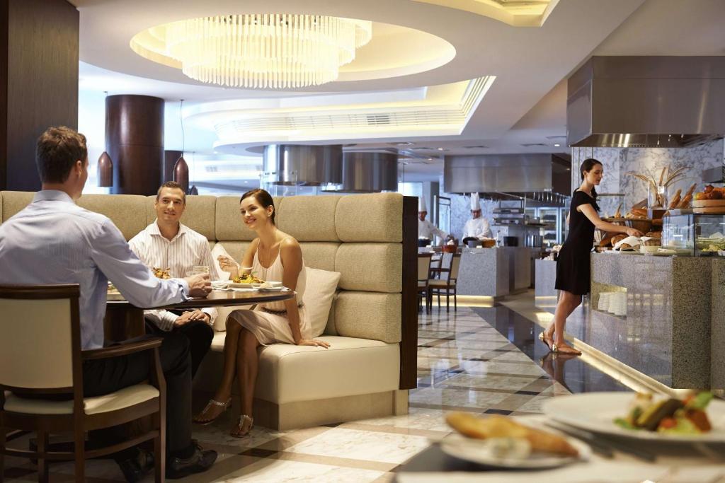 Moderns restorāns ar elegantu interjeru, kurā redzami apmeklētāji, kas bauda maltīti, un viesmīle, kas apkalpo. Gaisma un dizains veido patīkamu atmosfēru.