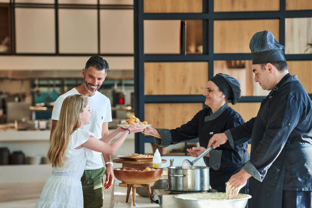 Ģimene baudīja maltīti restorānā, kur šefpavāri pasniedz ēdienus. Bērns saņem šķīvi ar uzkodām no pavāres, kamēr tēvs ar smaidu skatās.