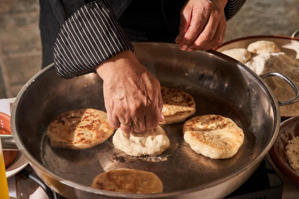 Sieviete gatavo plānās maizītes uz pannas, izmantojot rokās turētu mīklu. Ap pannu redzami dažādi maizīšu veidi un milti.