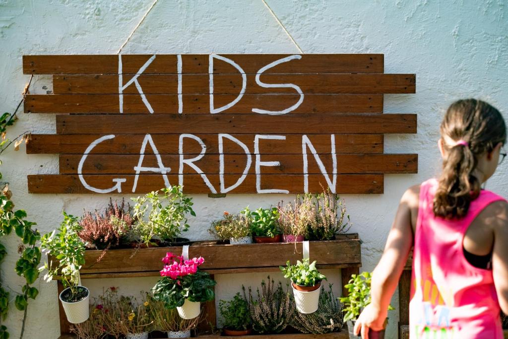 Bērnu dārzs ar koka zīmi un ziedu podiņiem, kas rotā sienu.