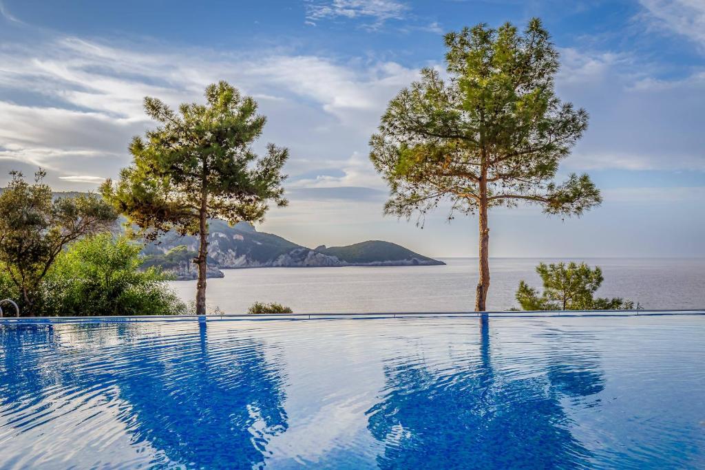 Ainava ar mierīgu baseinu, kas atspoguļo apkārtējo dabu, un kokiem, kas rotā skatu uz jūru un kalniem.