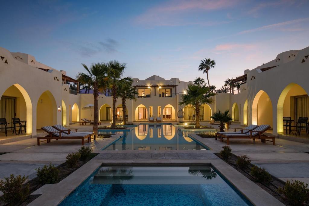 Xanadu Makadi Bay viesnīcas baseins ar palmām un apgaismojumu saulrieta laikā.
