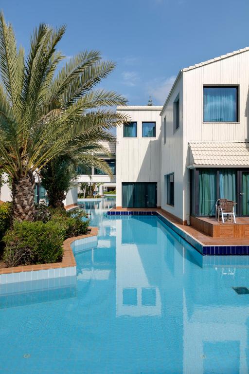 Susesi Luxury Resort baseins ar palmām un viesnīcas numuriem piekrastē.