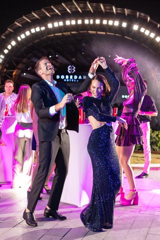 Priecīgi dejotāji Dobedan Exclusive Hotel & Spa pasākumā ar spožām gaismām.