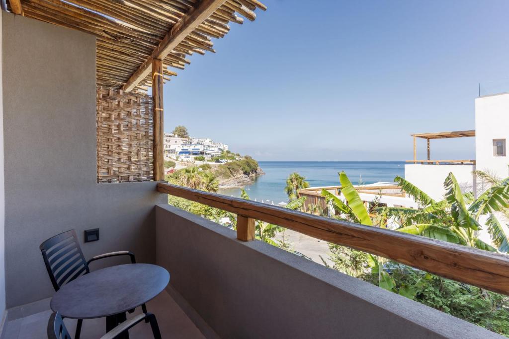 Balcony ar skatu uz jūru, kurā redzama ērtu krēslu un galda kombinācija, apkārt augošas palmas un piekrastes ainava.