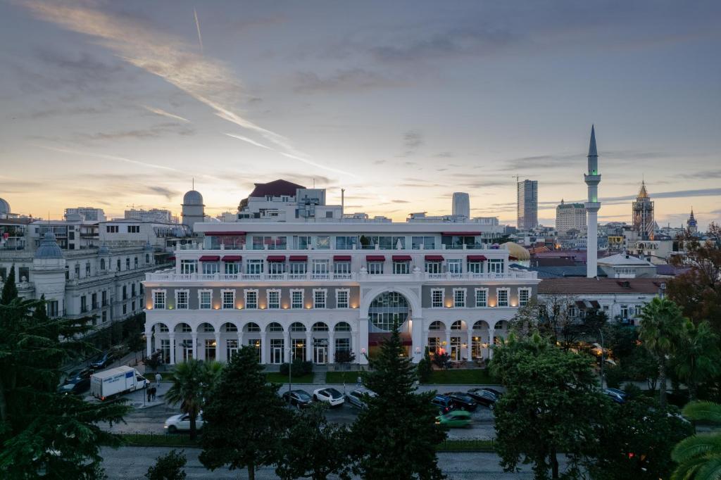 Pilsētas ainava ar elegantu arhitektūru un modernām ēkām, kurā redzams vēsturiskais viesnīcas komplekss un minarets, saulrieta gaismā.