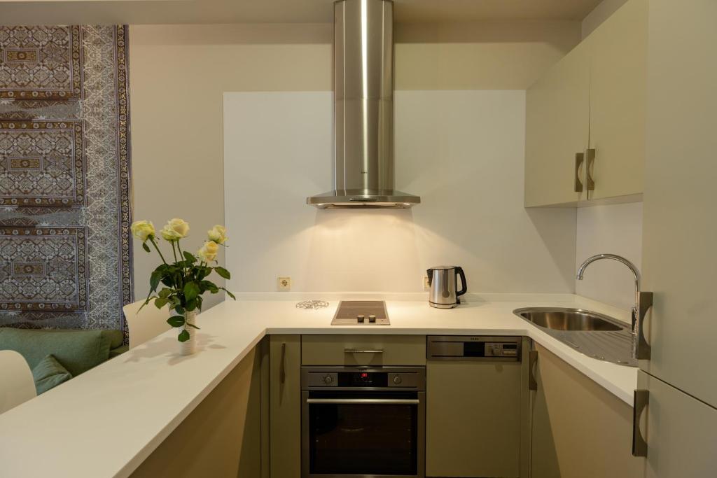 Mūsdienīga virtuve ar gaišām krāsām, plakanām virsmām un ziedu pušķi, kas piešķir dzīvīgumu. Dūmu izvadīšanas sistēma un aprīkojums, kas nodrošina ērtu gatavošanu.