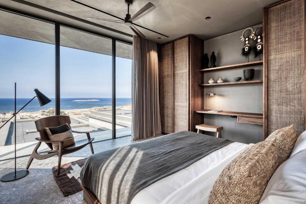 Mūsdienīgs guļamistabas interjers ar plašiem logiem, no kuriem paveras skats uz jūru. Istabā ir eleganta gulta, stilīgs krēsls un minimālistiski interjera elementi.