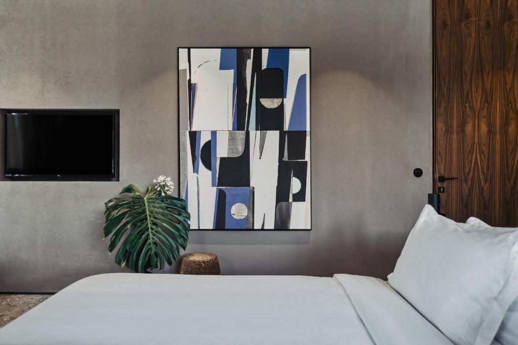 Moderns guļamistabas interjers ar abstraktu gleznu, televizoru un zaļu augu, radot mierīgu atmosfēru. Eleganta dizaina elementu kombinācija.