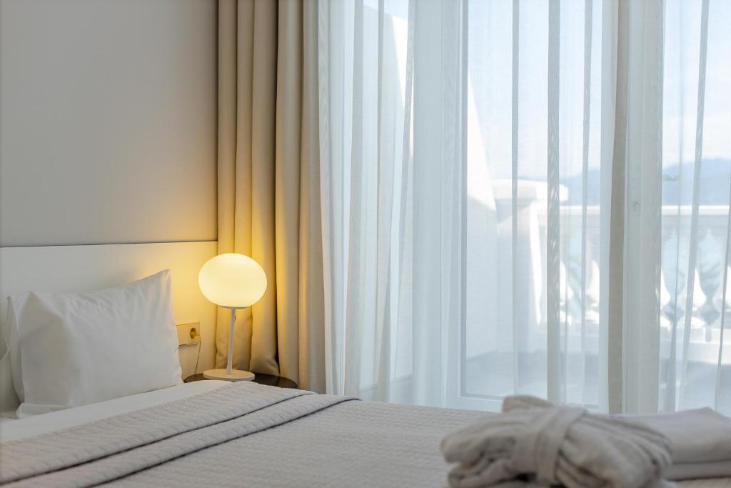 Mūsdienīgs guļamistabas interjers ar gaismu un smalkām aizkariem, kas sniedz mierīgu atmosfēru. Gultas veļa ir neitrālos toņos, radot relaksējošu noskaņu.