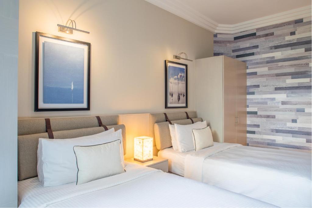 Mūsdienīgs guļamistabas interjers ar divām gultām, mīkstiem spilveniem un gaismu no naktslampām, papildināts ar mākslas darbiem uz sienām.