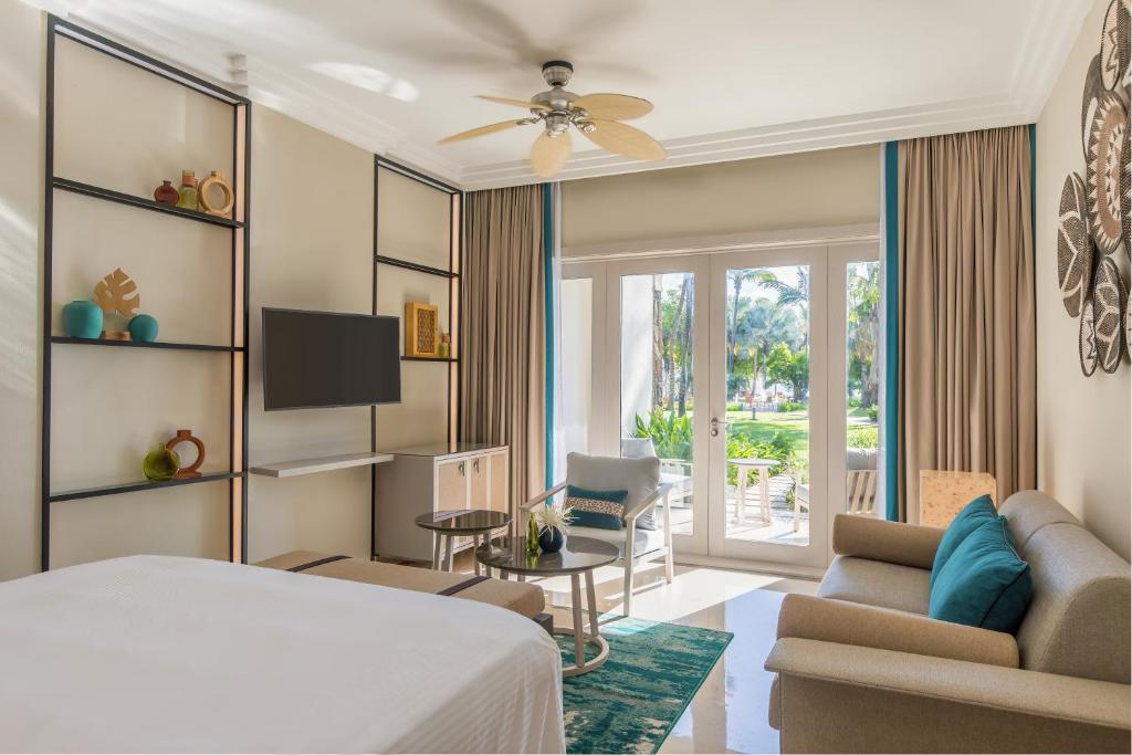 Mūsdienīgs viesnīcas numurs ar gaišiem toņiem, stilīgu mēbelēšanu un skatu uz dārzu. Telpā ir televizors, atpūtas zona un lieli logi, kas nodrošina dabisko apgaismojumu.